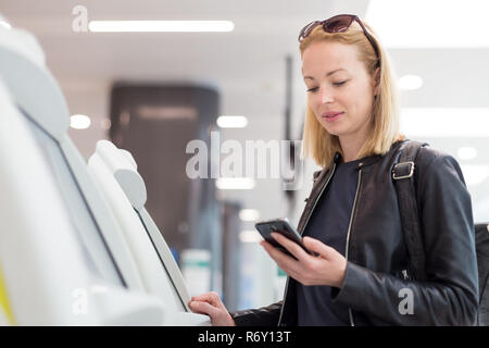 Casual kaukasische Frau mit Smart Phone Application und Check-in-Automaten am Flughafen erhalten der Bordkarte. Stockfoto