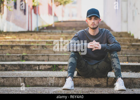 Modische junge Mann sitzt auf der Treppe in der Straße Stockfoto