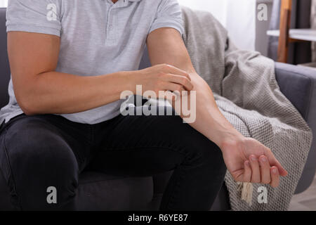 Mittelteil der Mann sitzt auf einem Sofa Juckreiz Leiden. Stockfoto