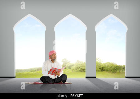 Senior asiatischen muslimischen Mann sitzt mit Koran Stockfoto