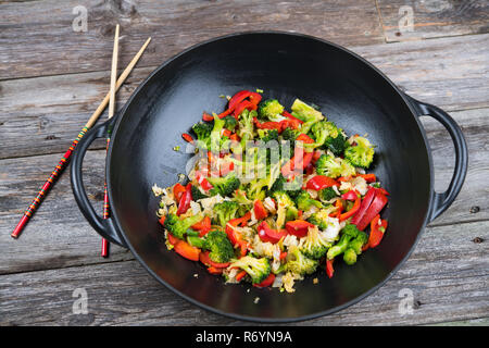 Wok mit Gemüse und Essstäbchen auf hölzernen Boden Stockfoto