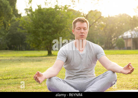 Jungen gutaussehenden Mann schließen Augen während der Meditation im Park Stockfoto