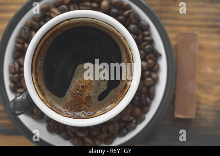 Eine Tasse Kaffee auf eine Untertasse mit gebratenen Kaffeebohnen und ein Stück Schokolade neben Stockfoto