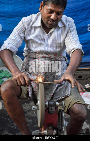 Ein Messerschärfer bei der Arbeit mit einem Wetzstein oder Schärfrad angetrieben über die Pedale eines Fahrrad-ähnlichen Mechanismus; Mumbai, Indien Stockfoto