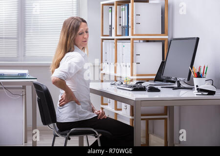 Seitliche Sicht auf eine Geschäftsfrau mit Rückenbeschwerden Stockfoto