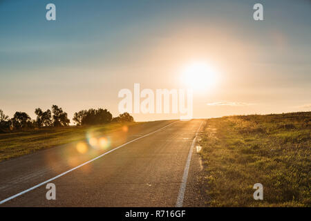 Sonnenaufgang über dem Asphalt Land Open Road im sonnigen Morgens oder abends. Straße In der Sommersaison bei Sunny Sunset Sunrise Stockfoto