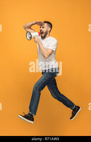 Springen Fan auf orangem Hintergrund. Der junge Mann als Fußball-Fußball-Fan mit Megafon Stockfoto