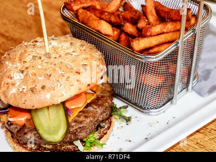 Lecker Cheese-Burger mit hausgemachten Süßkartoffel-Chips in einem kleinen Netz Warenkorb Stockfoto