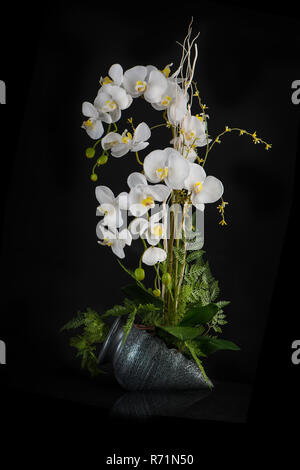 Tabelle Blumenschmuck aus künstlichen Orchideenblüten in stilisierten Keramik Vase auf weißem Hintergrund. Stockfoto