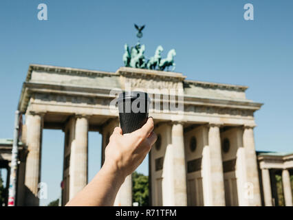Eine Person hält eine Tasse mit Kaffee oder einem anderen Getränk auf dem Hintergrund der Brandenburger Tor in Berlin in Deutschland bei einem Spaziergang oder beim Sightseeing. Stockfoto