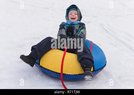 Fröhlicher schöner Junge Reiter der Achterbahn. Kleinkind Wandern im Schnee im Winter. Das Kind lacht und lächelt in Winter Park. Stockfoto