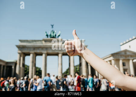 Eine Person zeigt ein Zeichen mit dem Finger nach oben Sinne alles in Ordnung ist oder bestätigt vor dem Hintergrund des Brandenburger Tor und verschwommenes unkenntlich Menschen in Berlin in Deutschland. Stockfoto