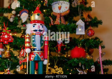 Große Dose Nussknacker Soldat auf einem Weihnachtsbaum mit verschwommenen Hintergrund. Saisonale Spielzeug Figur vor einer beleuchteten künstlicher Weihnachtsbaum. Stockfoto