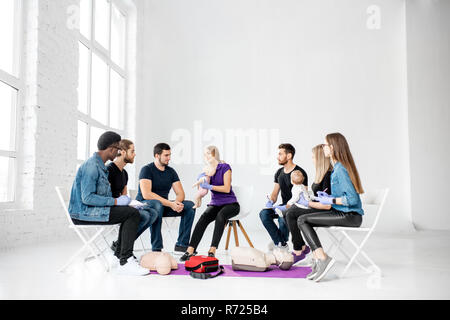 Gruppe von Menschen, die während der Schulung in erster Hilfe mit Instruktor an der Prüfpuppe wie künstliche Beatmung für das Baby tun Stockfoto