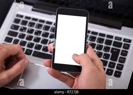 Mann mit Handy mit leeren weißen Bildschirm über Laptop Stockfoto