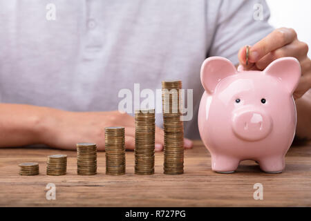 Mann einfügen Münze in Sparschwein in der Nähe von steigenden Gewinn Stockfoto