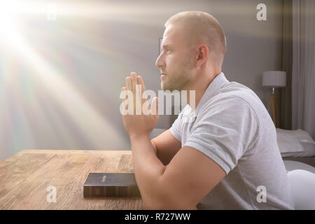 Seitenansicht eines jungen Mannes Beten mit Bibel über Holz- Schreibtisch zu Hause Stockfoto