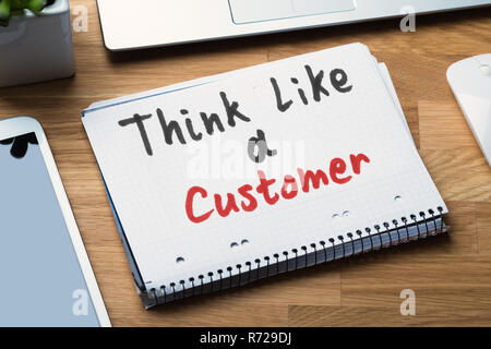 Denken wie ein Kunde Text auf Spiral Notizblock mit Elektronische Geräte auf dem Schreibtisch geschrieben Stockfoto