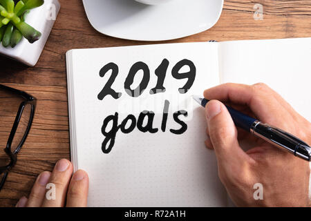 Nahaufnahme einer Person die Hand Schreiben 2019 Jahr Ziele auf Gepunktete Notebook über Holz- Schreibtisch Stockfoto