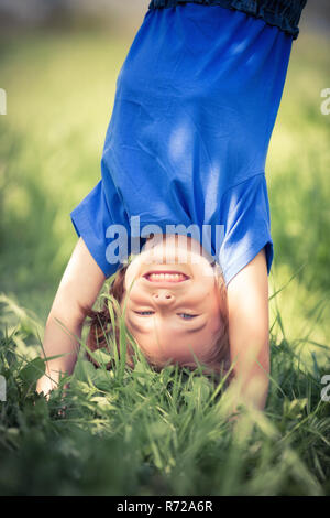 Glückliche kleine Mädchen stehen auf dem Kopf stehend auf dem Rasen im Sommerpark Stockfoto