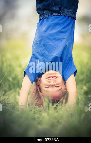 Glückliche kleine Mädchen stehen auf dem Kopf stehend auf dem Rasen im Sommerpark Stockfoto