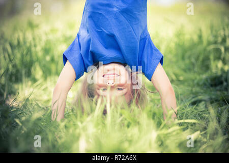 Glückliche kleine Mädchen stehen auf dem Kopf stehend auf dem Rasen im Sommerpark Stockfoto