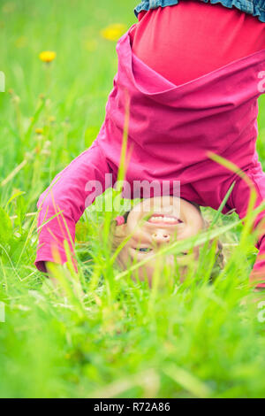 Glückliche kleine Mädchen stehen auf dem Kopf stehend auf dem Rasen im Sommerpark Stockfoto