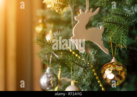 Rotwild Spielzeug auf dem Weihnachtsbaum. Goldene Kugeln, Perlen, andere Dekorationen. Neues Jahr Thema Konzept. Sonne orange getönt. Stockfoto