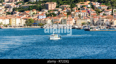 Panoramablick auf Mali Losinj Hafen und Stadt in Kroatien. Angeln Boot verlässt den Hafen mit vielen anderen Boote, Segel Schiffe und Altstadt Gebäude. in t Stockfoto