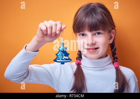 Spielzeug für den Weihnachtsbaum an der kaukasischen Mädchen in der Hand auf einem farbigen Hintergrund, Platz für Text Stockfoto