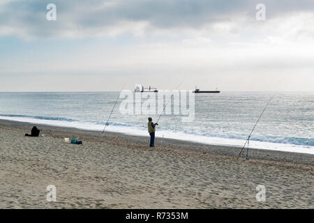 Savona, Italien, 25. Oktober 2018: ein Fischer mit der Angelrute in der Hand versucht, einen Fisch zu erholen, die er zu den beiden anderen Angelruten pos Stockfoto