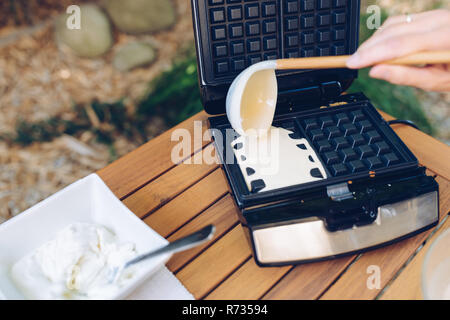 Zubereitung von hausgemachten Waffeln. Gießen Teig in das Waffeleisen mit einer Schöpfkelle draußen im Garten Stockfoto