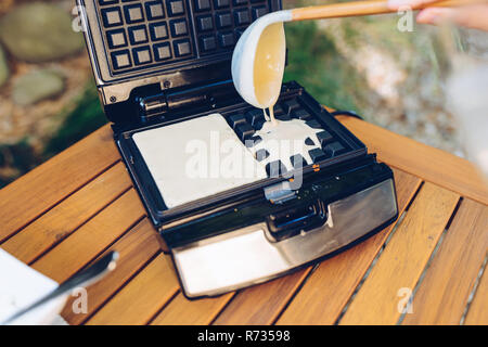 Zubereitung von hausgemachten Waffeln. Gießen Teig in das Waffeleisen mit einer Schöpfkelle draußen im Garten Stockfoto