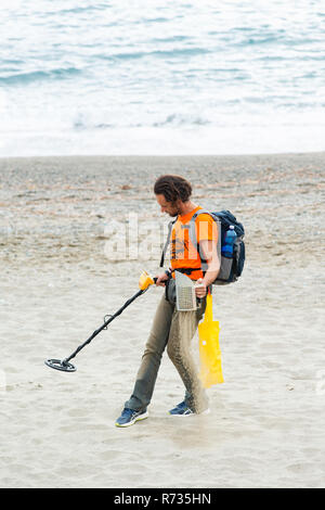 Savona, Italien, 25. Oktober 2018: Der Mann ist zu Fuß am Strand mit einem Metalldetektor in der einen Hand und ein Sieb in der anderen. Er versucht zu finden, Jewe Stockfoto