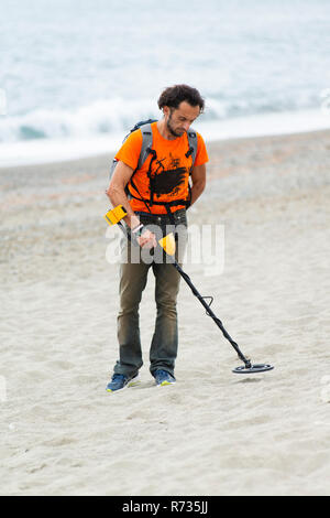 Savona, Italien, 25. Oktober 2018: Der Mann ist zu Fuß am Strand mit einem Metalldetektor in der einen Hand und ein Sieb in der anderen. Er versucht zu finden, Jewe Stockfoto