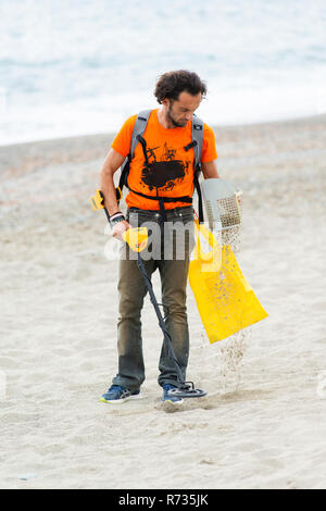 Savona, Italien, 25. Oktober 2018: Der Mann ist zu Fuß am Strand mit einem Metalldetektor in der einen Hand und ein Sieb in der anderen. Er versucht zu finden, Jewe Stockfoto