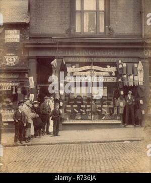 Edwardian Foto von J.A.S (James) Illingworth Juvenile Outfitters, Schneider und Textilhändler. 18 Attercliffe Road, Sheffield, South Yorkshire, England, Großbritannien Assistenten/Personal und Kunden aus dem Supermarkt nebenan haben auch für das Foto, während der Eigentümer der Schneider ein würdiges und humorlosen Pose unterhält. Circa 1905. Stockfoto