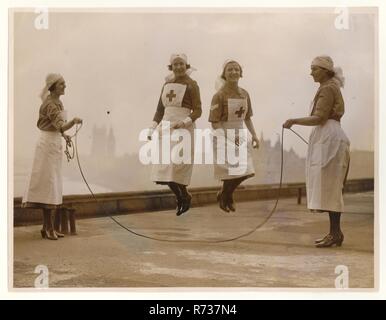 Junge freiwillige Krankenschwestern aus dem 2. Weltkrieg, die oben auf einem Gebäude in London, Westminster im Hintergrund, mit Voluntary Aid Detachment (VAD) Uniform um 1940, London, Großbritannien, springen/entspannen Stockfoto
