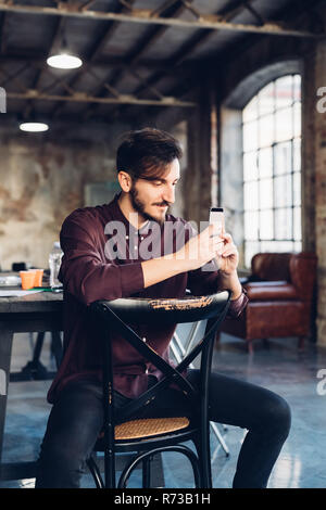 Mann sitzt hinten nach vorne am Stuhl mit Smartphone Stockfoto