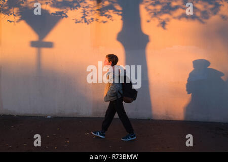Ein elfjähriger Junge mit Rucksack Spaziergänge entlang einer Mauer, mit Schatten bedeckt, auf seinem Weg in den frühen Morgenstunden in Montpellier, Frankreich zur Schule Stockfoto