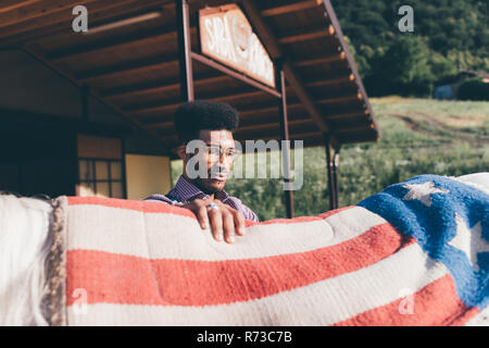 Junger Mann setzen amerikanische Flagge Decke auf dem Rücken des Pferdes an der Ranch Stockfoto