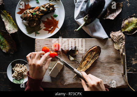 Frau slicing Kirschtomaten auf rustikalen Schneidebrett, Ansicht von oben der Hände Stockfoto