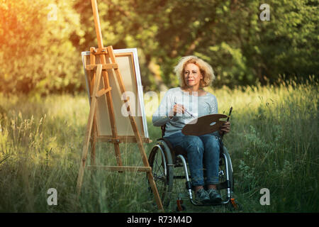 Frau im Rollstuhl Zeichnung auf staffelei außerhalb Stockfoto