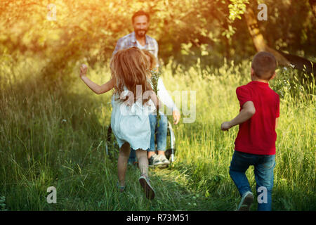 Kinder laufen für ihre behinderte Mutter im Park Stockfoto