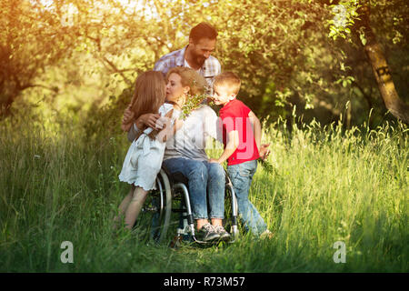 Frau im Rollstuhl küsst ihr Sohn unter Familienmitgliedern Stockfoto