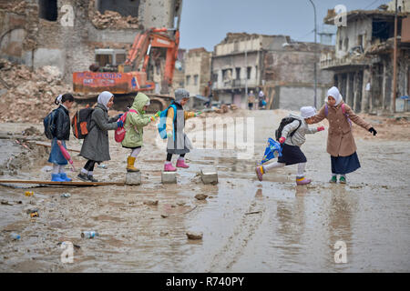 Mädchen Navigieren in einer schlammigen Straße, wie sie ihren Weg inmitten der Trümmer der Alten Stadt Mosul, Irak, die während der 2017 Ba verwüstet wurde, zur Schule Stockfoto