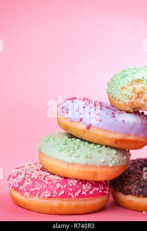 Süße bunte leckere Krapfen mit Puderzucker und Streuseln auf Pastell rosa Hintergrund. Stockfoto