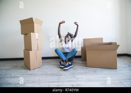 Menschen, neuen Platz und Reparatur Konzept - glückliche afrikanische amerikanische junge Frau mit vielen Kartons sitzen auf dem Boden zu Hause Stockfoto