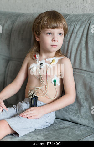 Kind auf dem Sofa sitzen. Herz Elektrokardiogramm oder Überwachung der Herzfunktion mit Holter. Stockfoto