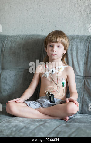 Kind auf dem Sofa sitzen. Herz Elektrokardiogramm oder Überwachung der Herzfunktion mit Holter. Stockfoto